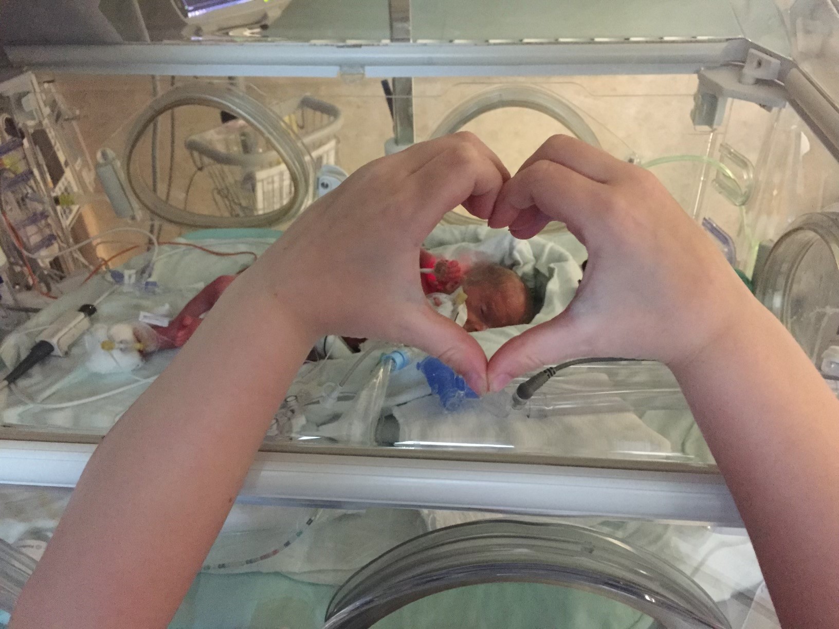 Michael framed by hands held in the shape of a heart while in the NICU.