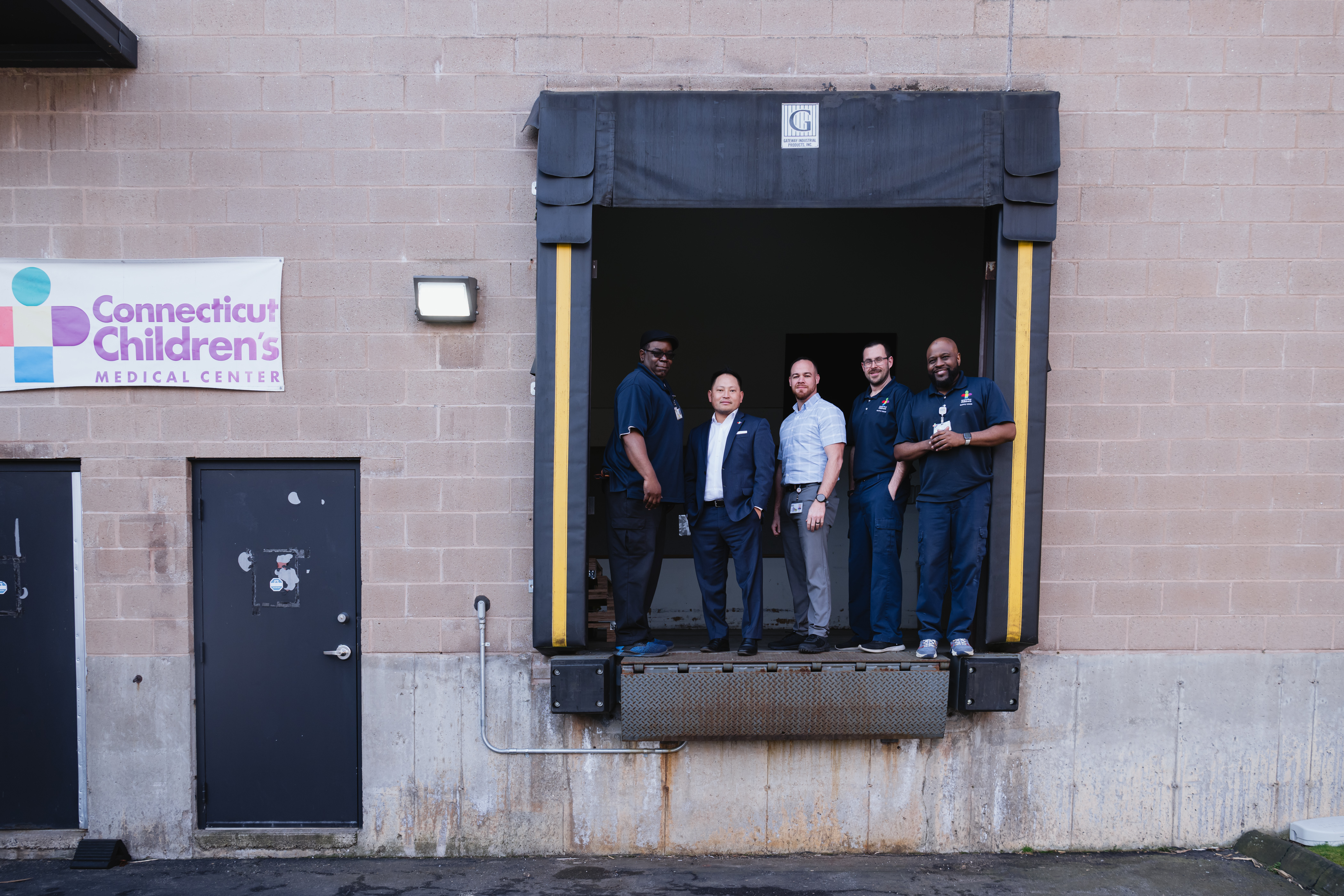 Will Lee, Director, Supply Chain, at Connecticut Children’s with Supply Chain team members, standing on a warehouse loading dock bay..