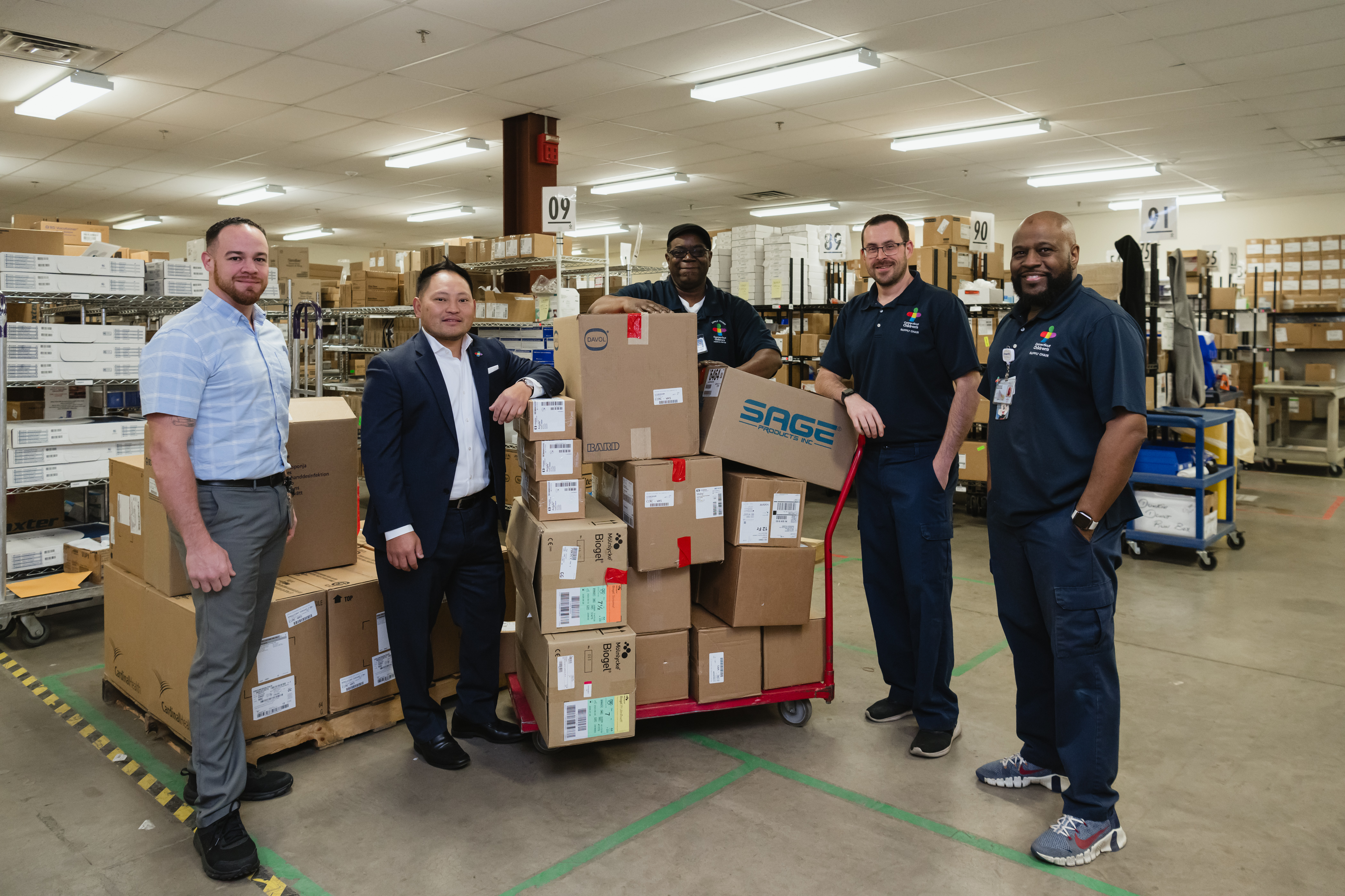 Will Lee, Director, Supply Chain, at Connecticut Children’s, standing with Supply Chain team members in the warehouse.