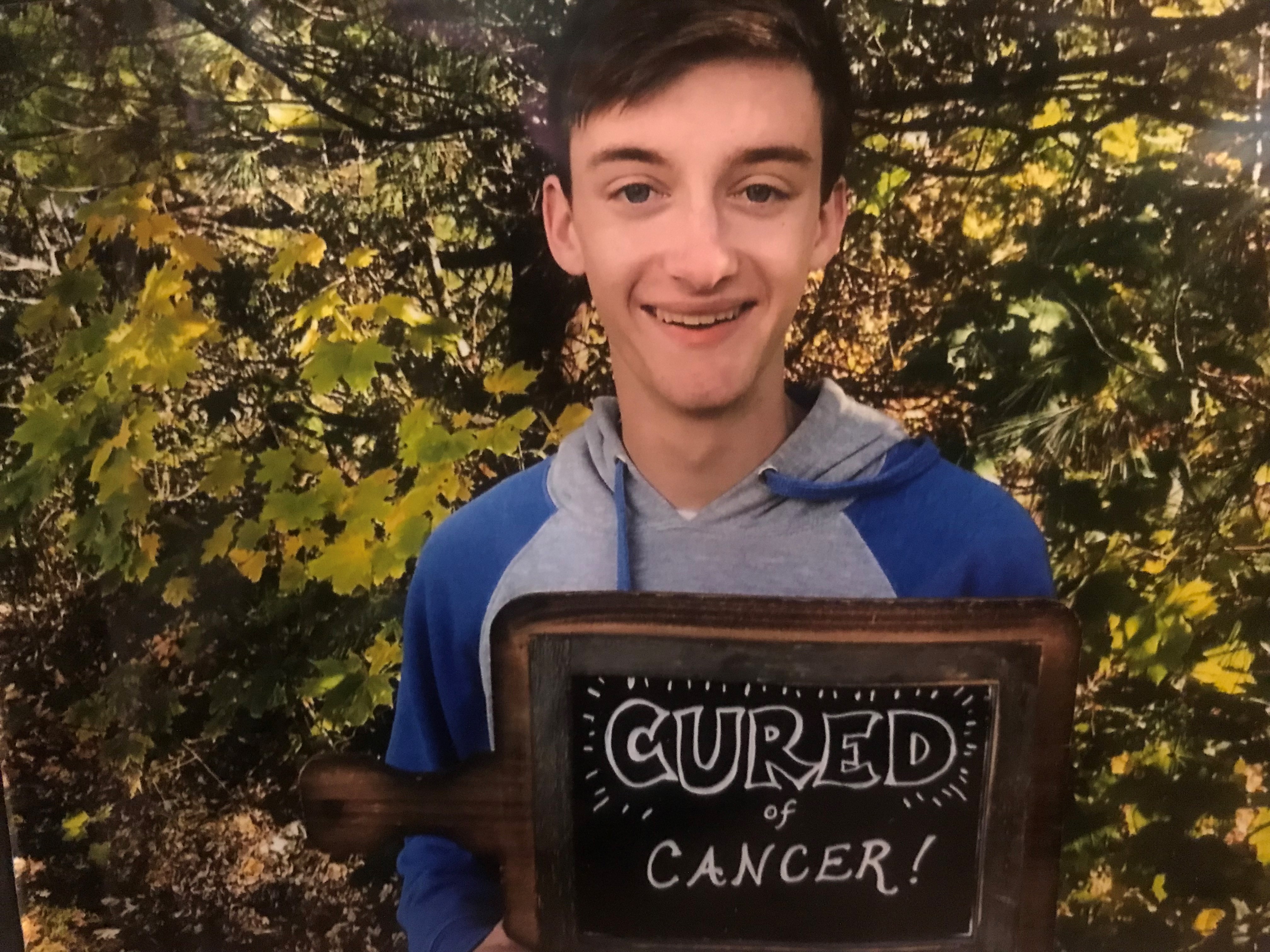 Isaac, holding a sign that says "Cured of Cancer!"