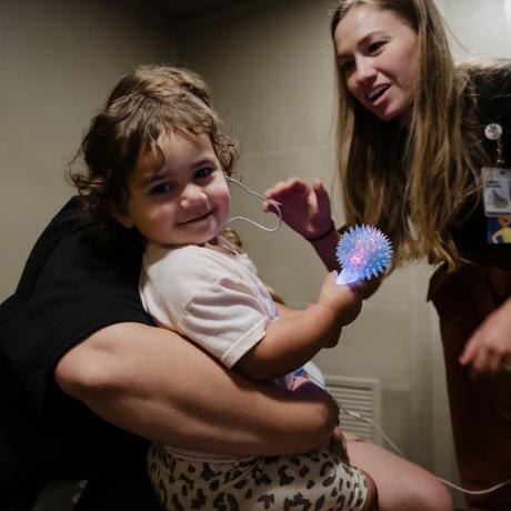 A toddler is seen by Audiology. She holds a distraction toy, provided by Child Life.