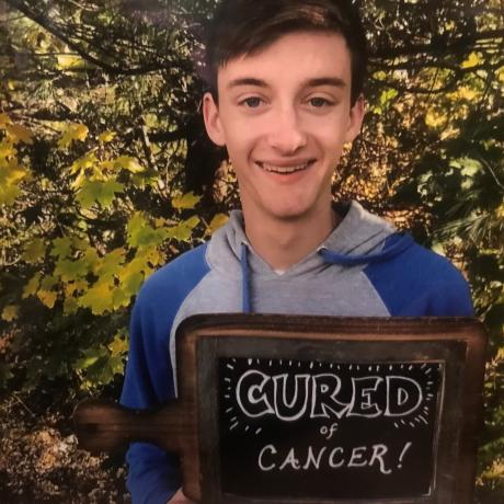 Isaac, holding a sign that says "Cured of Cancer!"