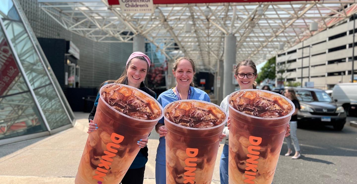 Nurses hold up giant Dunkin' Iced Coffee cutouts to celebrate Dunkin' Iced Coffee Day.