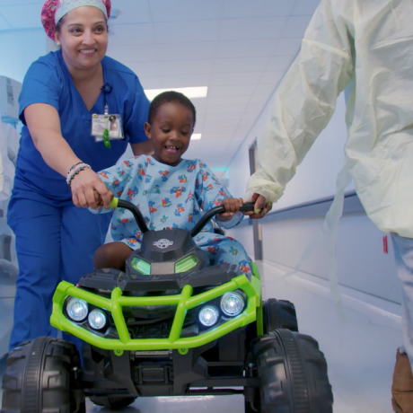 Child life specialists helps child patient drive his toy car down to surgery